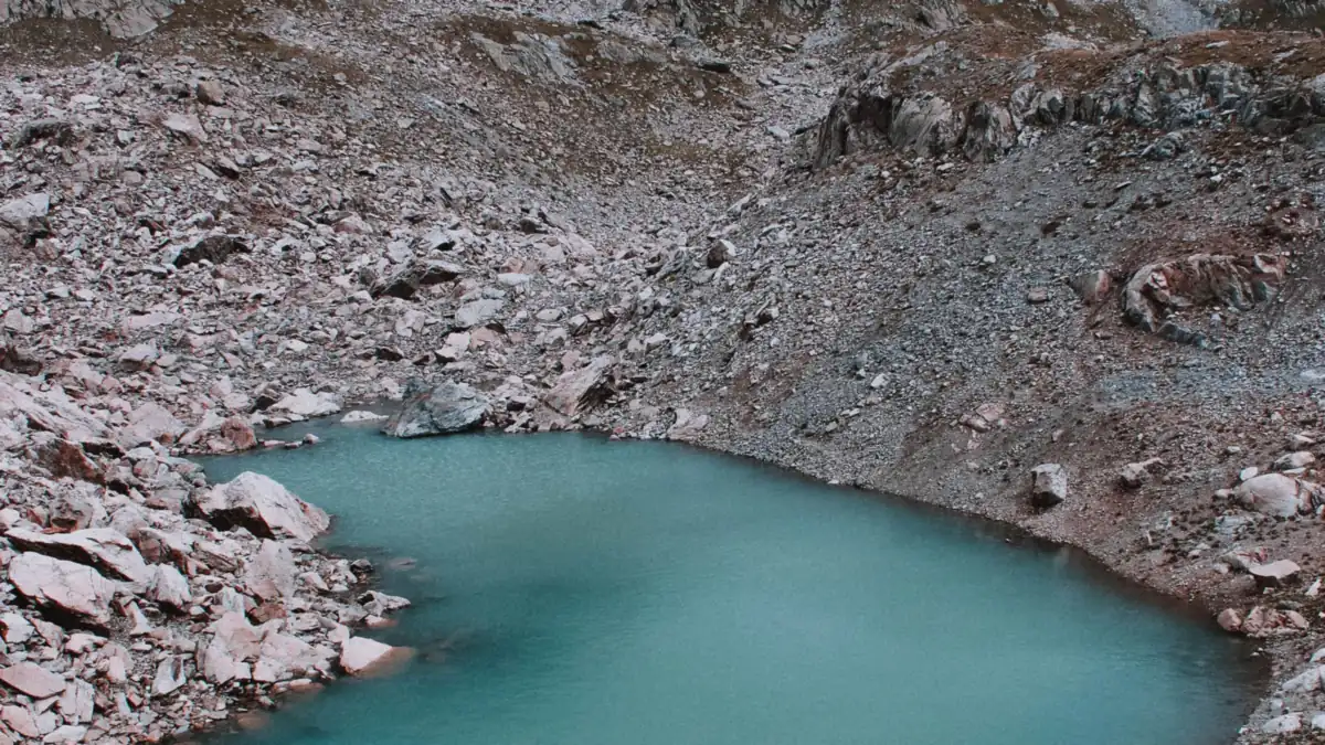 A still blue lake held in a bare rock basin high above the treeline under a pale sky