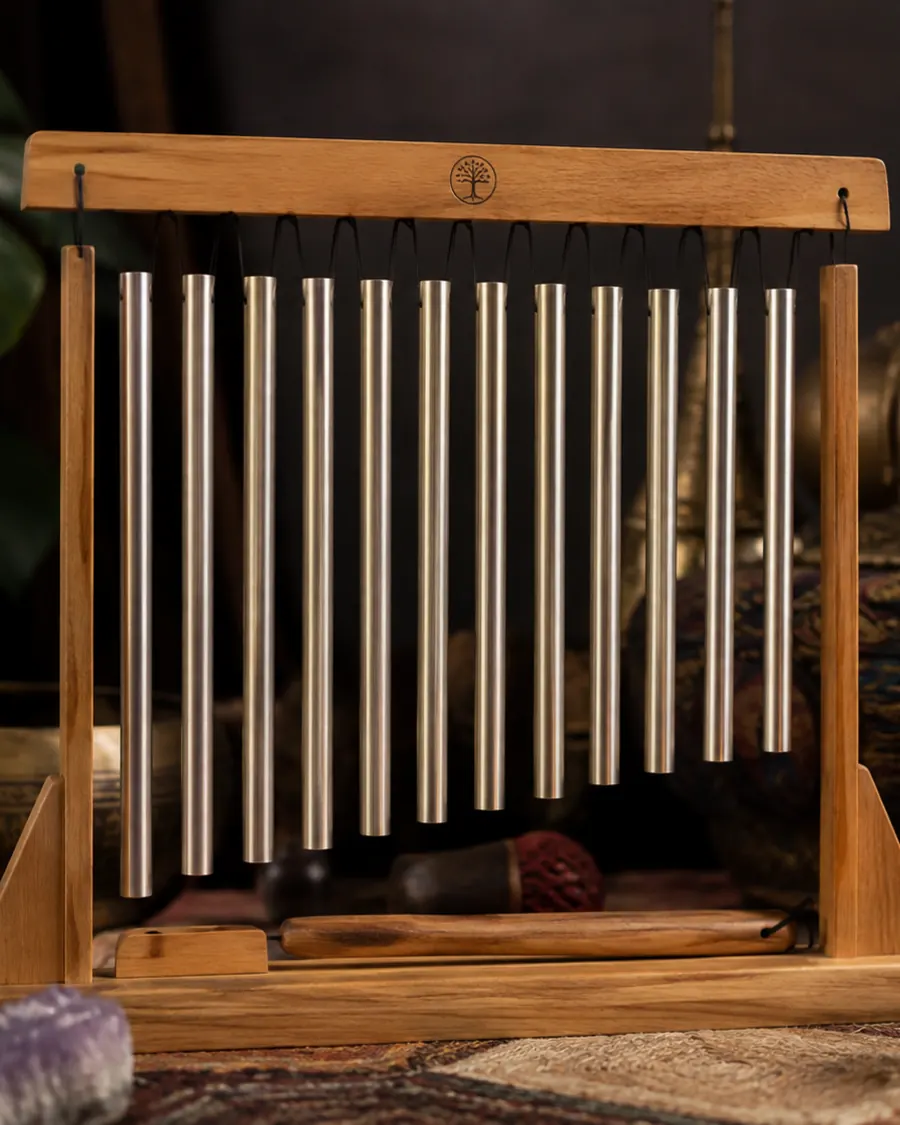 A wooden frame of hanging sound-healing chimes beside a singing bowl and a lit candle in warm low light