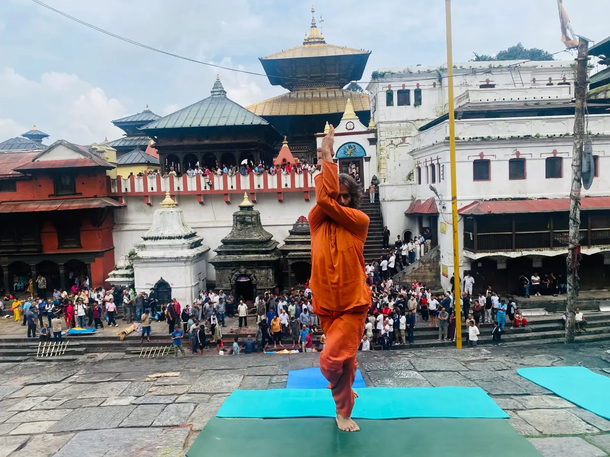 Yogi Ji standing in a balance on a mat in the courtyard of Pashupatinath, the pagoda and a crowd of several hundred behind him