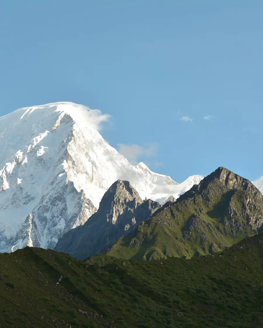 A snow-covered Himalayan peak catching the first light of morning above dark ridges